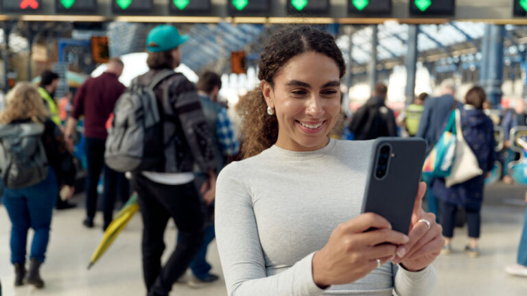 EE official image showing a mobile user at a busy UK station for 5G Plus network coverage