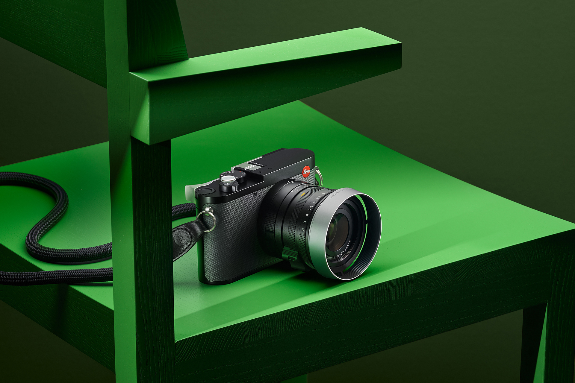 Leica Q3 43 black compact camera resting on a green chair with its strap hanging down
