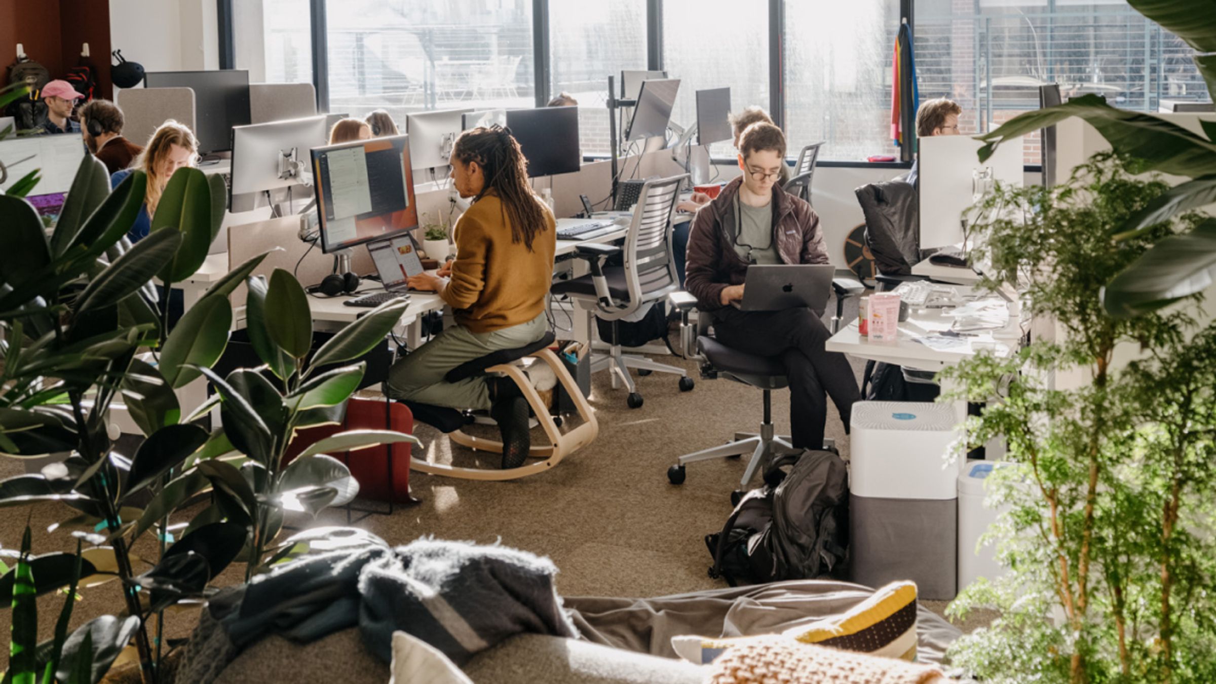Open-plan London AI research office with staff at desks, plants and floor-to-ceiling city windows