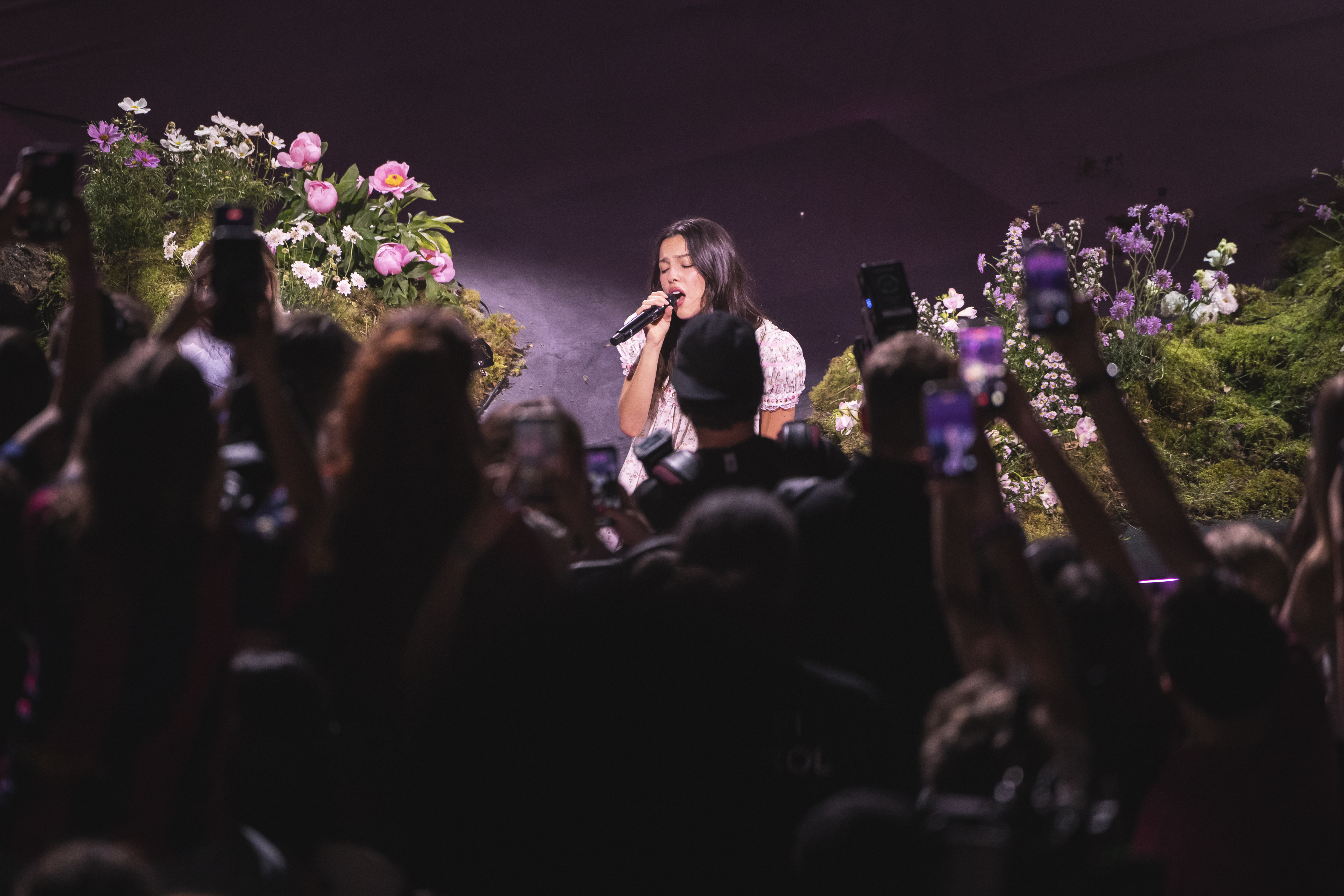 Fans holding up phones to film Olivia Rodrigo singing on a flower-framed stage in Barcelona