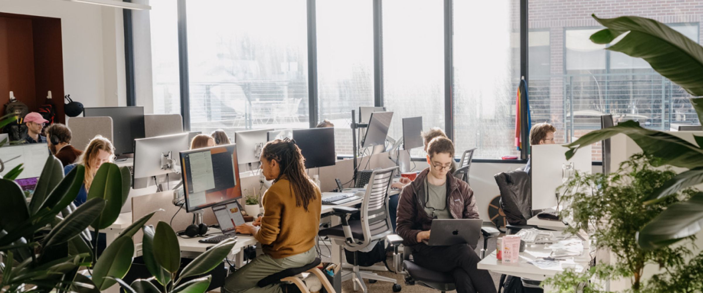 Researchers at desks in a daylit AI office with city skyline visible through the windows