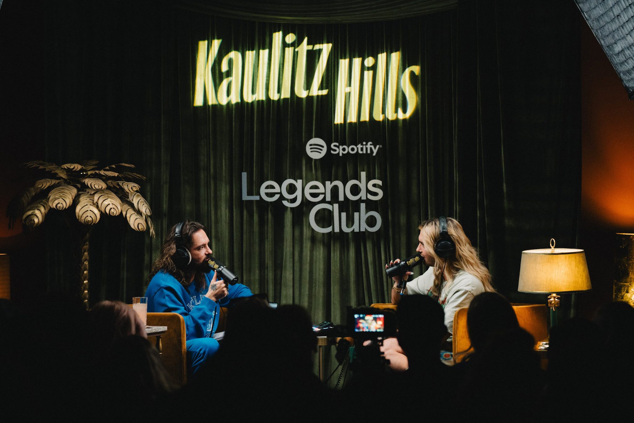 Two podcast hosts recording a video podcast with microphones and headphones on a Spotify set