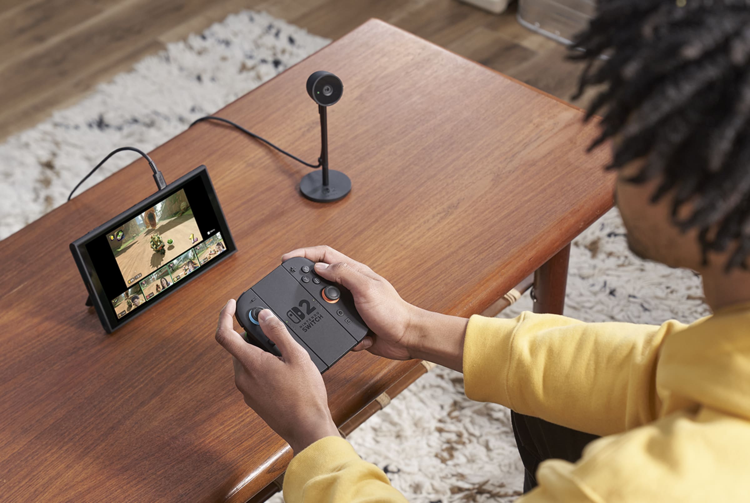 A player holding the Joy-Con 2 grip while the Nintendo Switch 2 sits in tabletop mode beside its camera, running a multiplayer Mario Kart World race