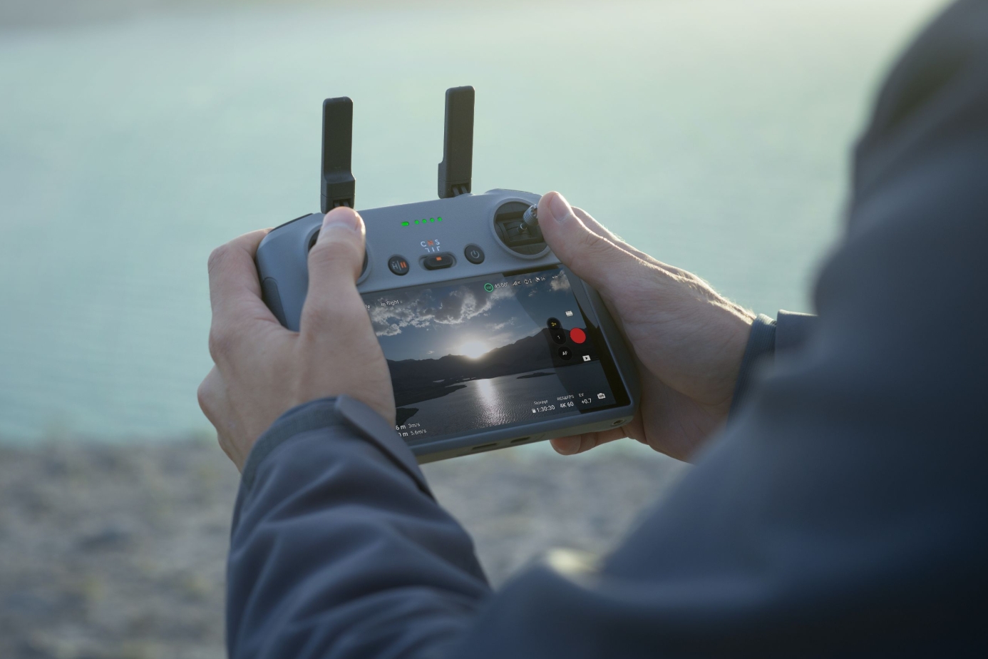 Pilot holding the DJI RC 2 controller with built-in screen showing a live drone feed outdoors