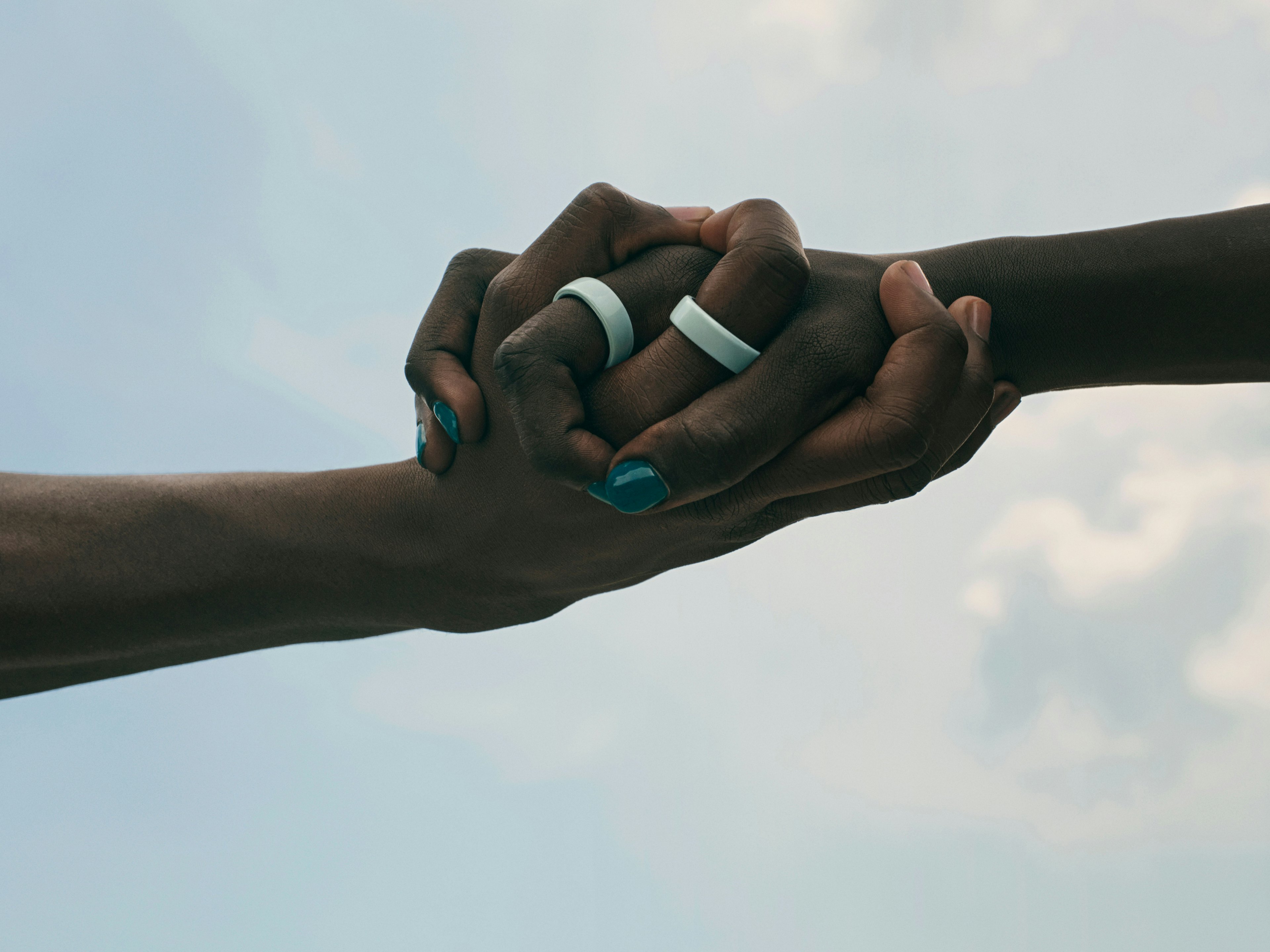 Two people wearing Oura smart rings on clasped hands against the sky
