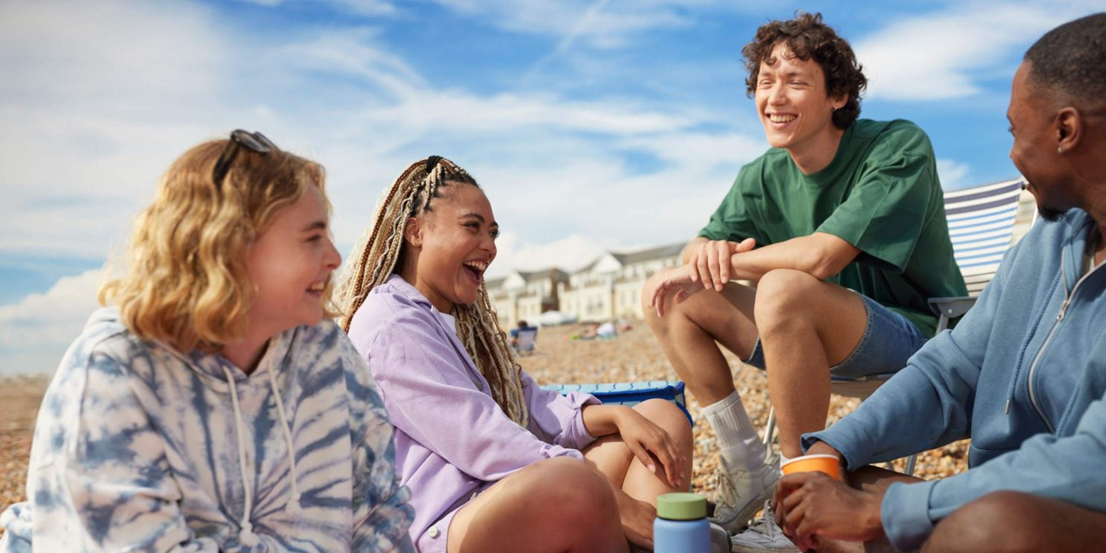 Four friends laughing together on a pebble beach, a Three UK lifestyle scene