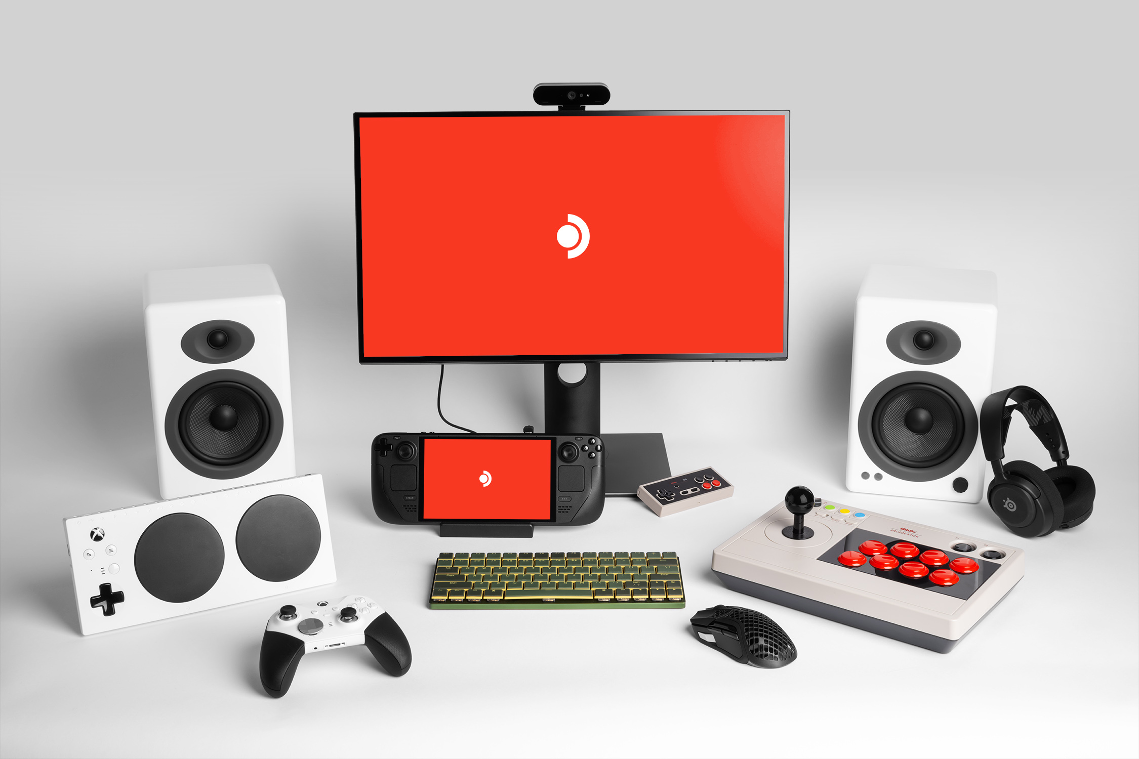 Steam Deck OLED docked to a monitor surrounded by speakers, keyboard, mouse, controllers and a headset