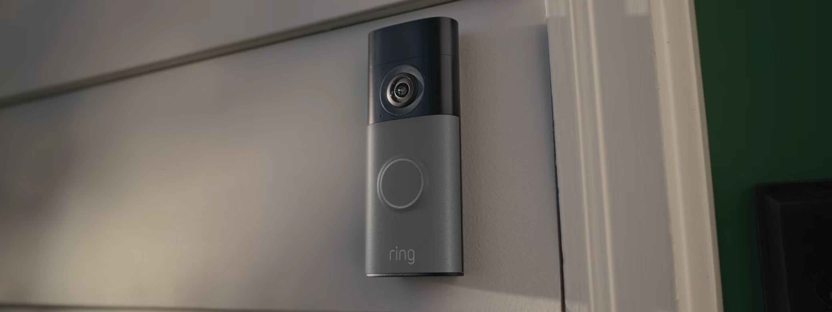 Ring battery doorbell mounted on grey wall in close-up showing the camera lens and button