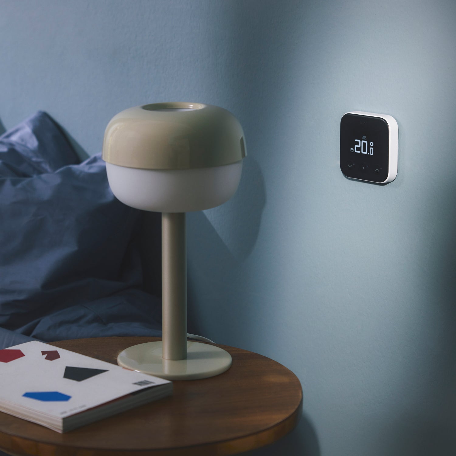 A tado Smart Thermostat X mounted on a bedroom wall near a bed in soft morning light