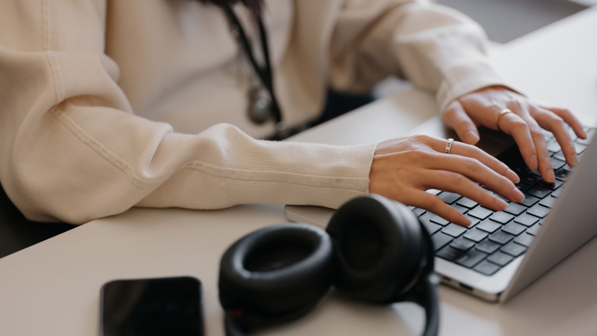 Person typing on a laptop at a desk with over-ear headphones and a phone alongside