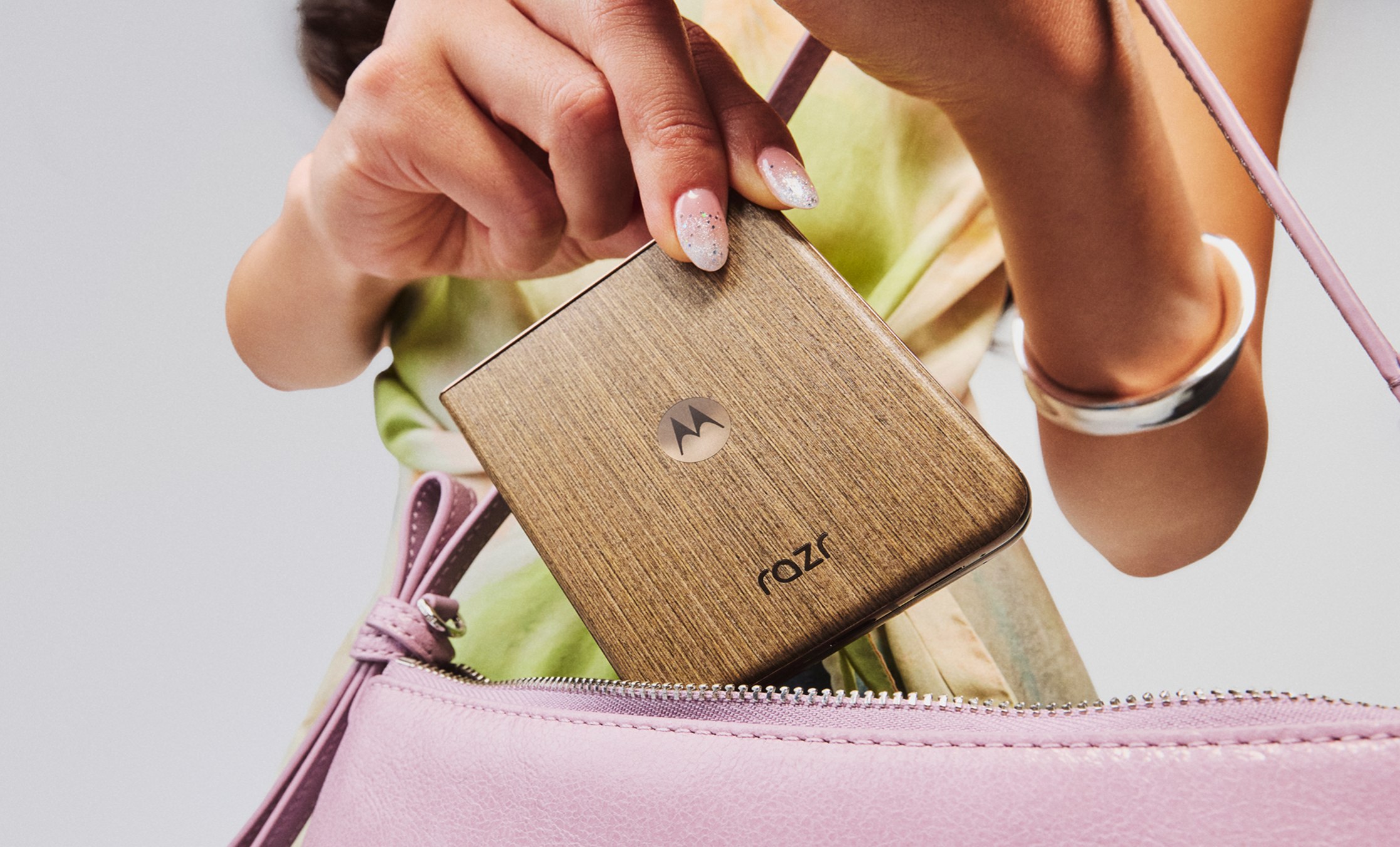 Motorola Razr 70 Ultra in its wood-effect finish, closed, being slipped into a handbag