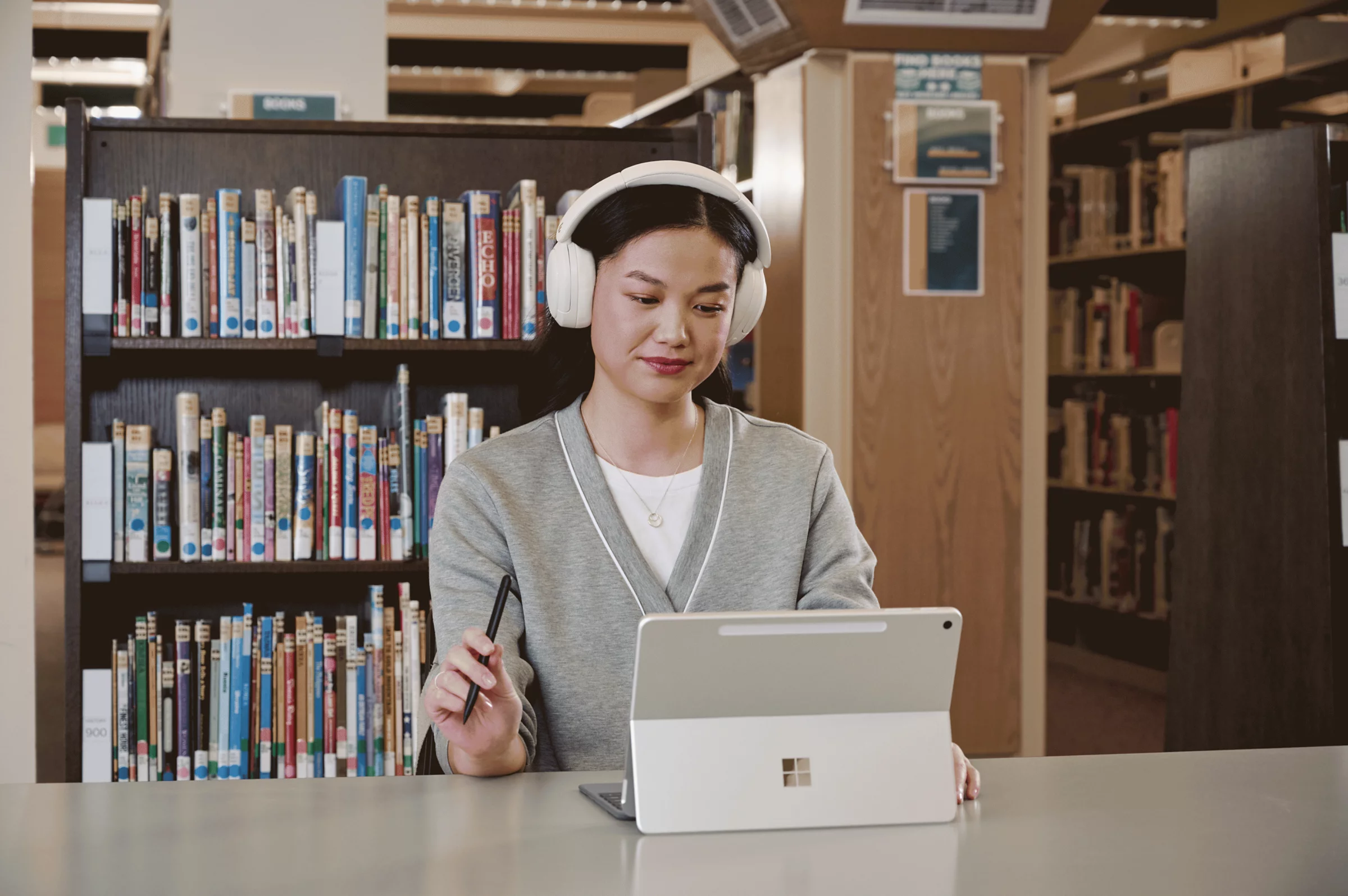 Student using a Microsoft Surface Pro with headphones at a desk in a library