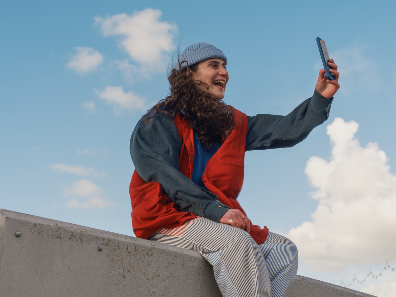 A young phone user outdoors checking a handset, representing pay-as-you-go and SIM-only customers avoiding mid-contract rises