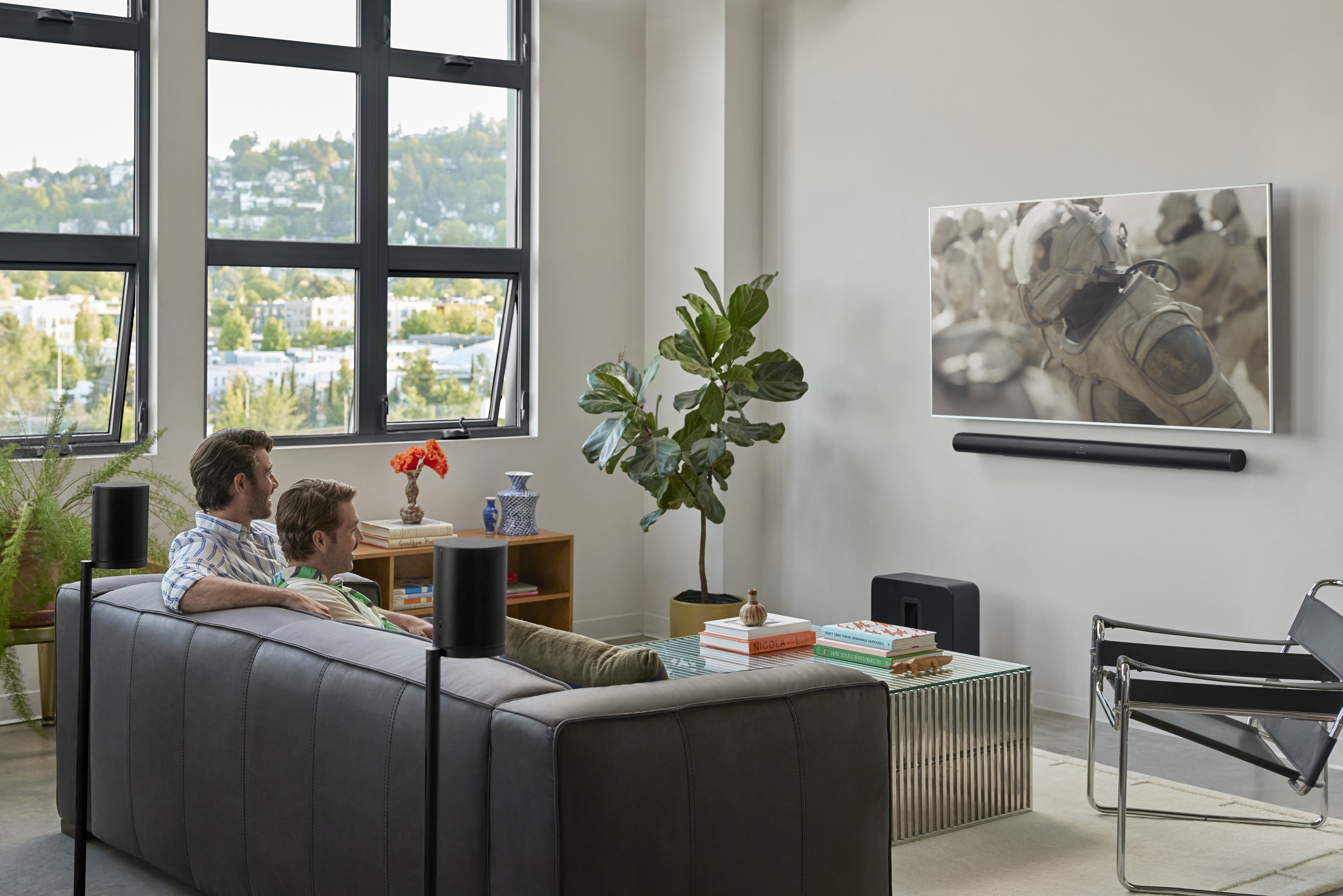 Two people watching a wall-mounted TV with a Sonos Arc Ultra, Sub 4 and Era 100 speakers in a loft living room