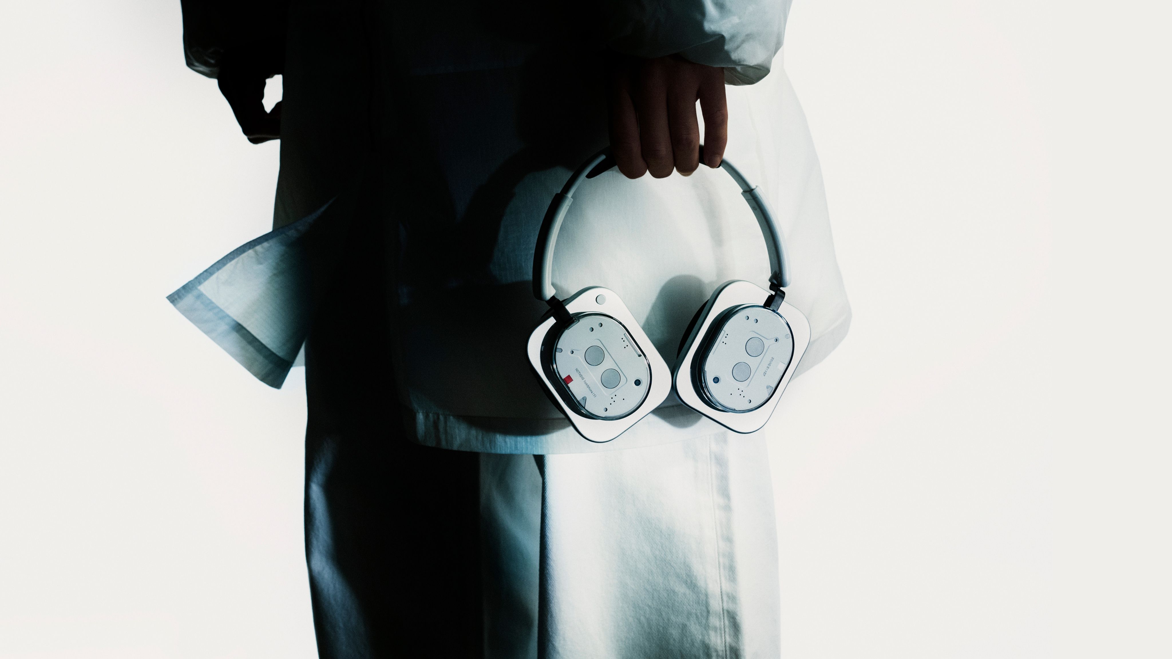 Person holding the white Nothing Headphone (1) by the headband showing the aluminium earcups