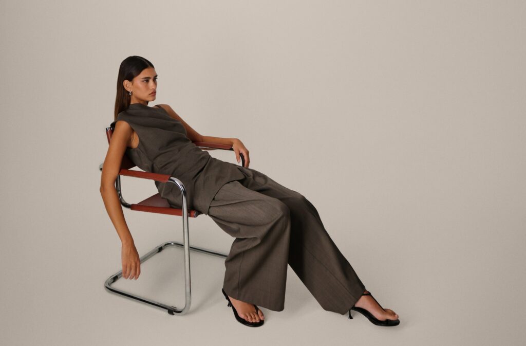 ASOS model in brown sleeveless top and wide-leg trousers reclining on a tubular steel chair