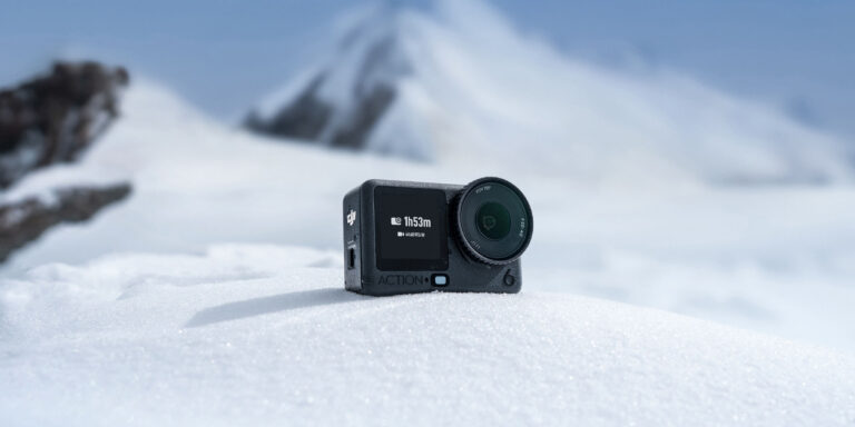 DJI Osmo Action 6 action camera resting on snow with a mountain backdrop