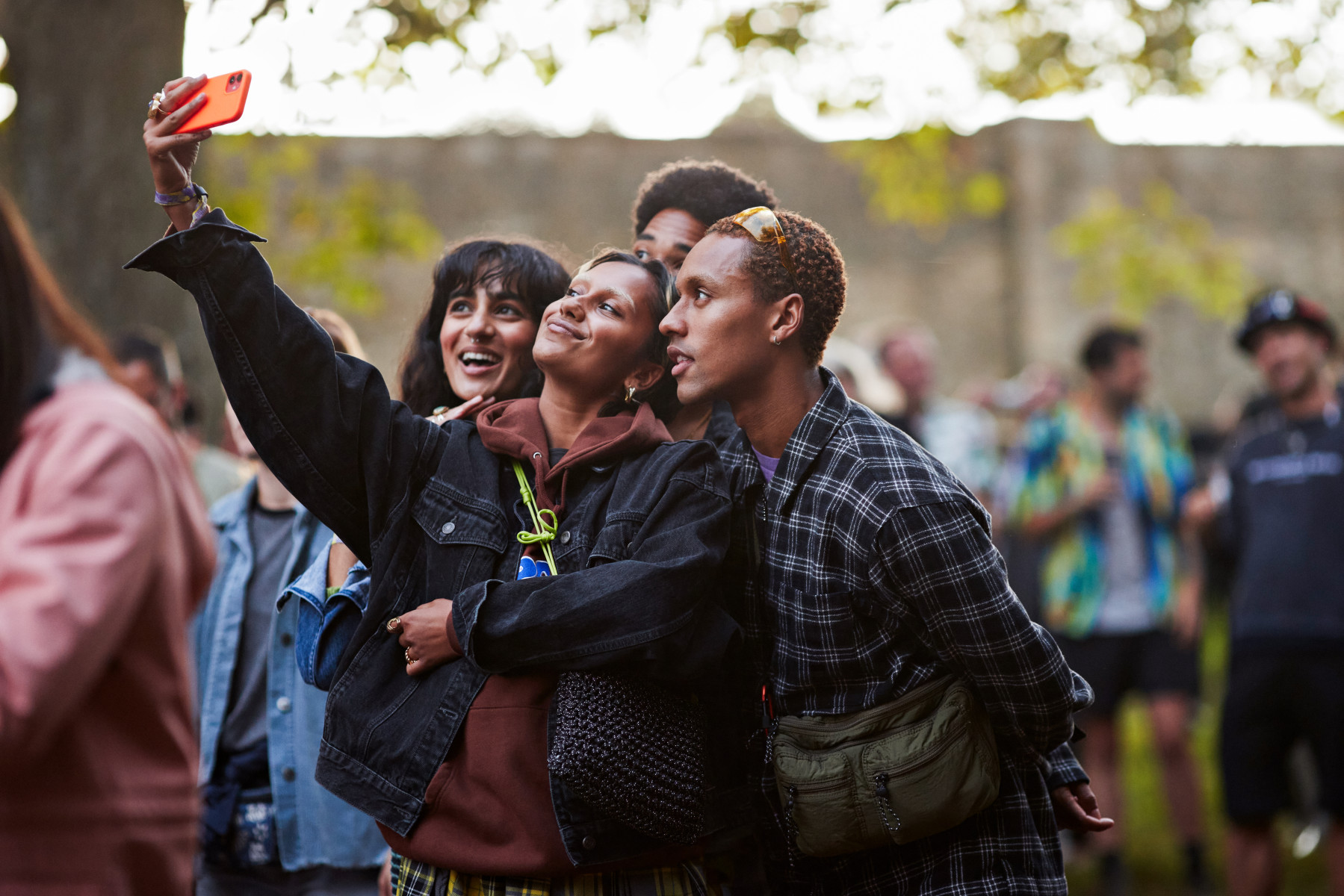 Young friends taking a selfie on a red smartphone at a crowded outdoor event