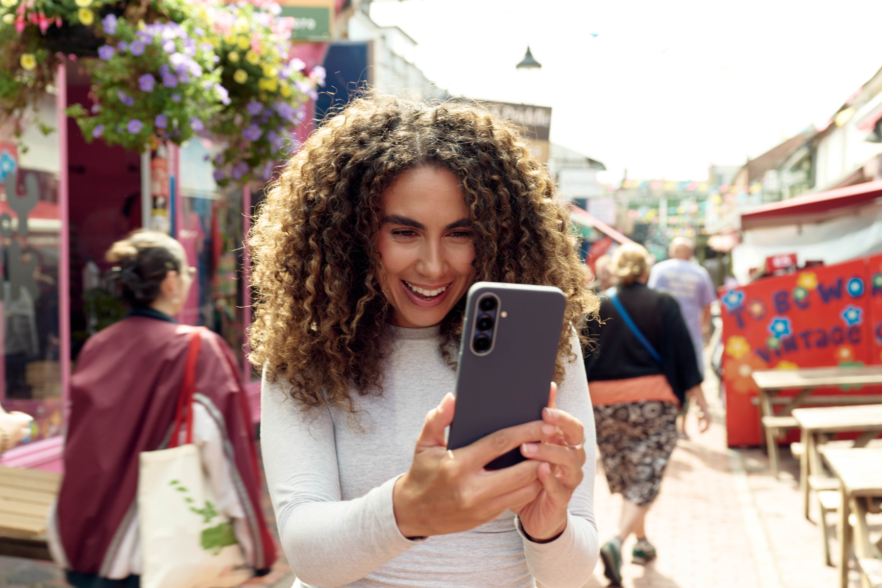 Smiling woman holding a smartphone on a colourful Brighton street with shops behind