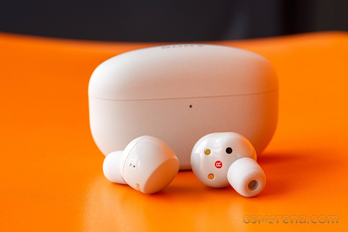 Sony WF-1000XM5 white earbuds in front of the charging case on an orange surface