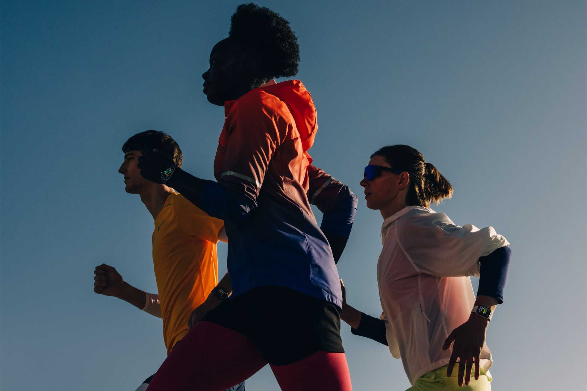 Three runners against a blue sky each wearing an Apple Watch Series 11 on the wrist