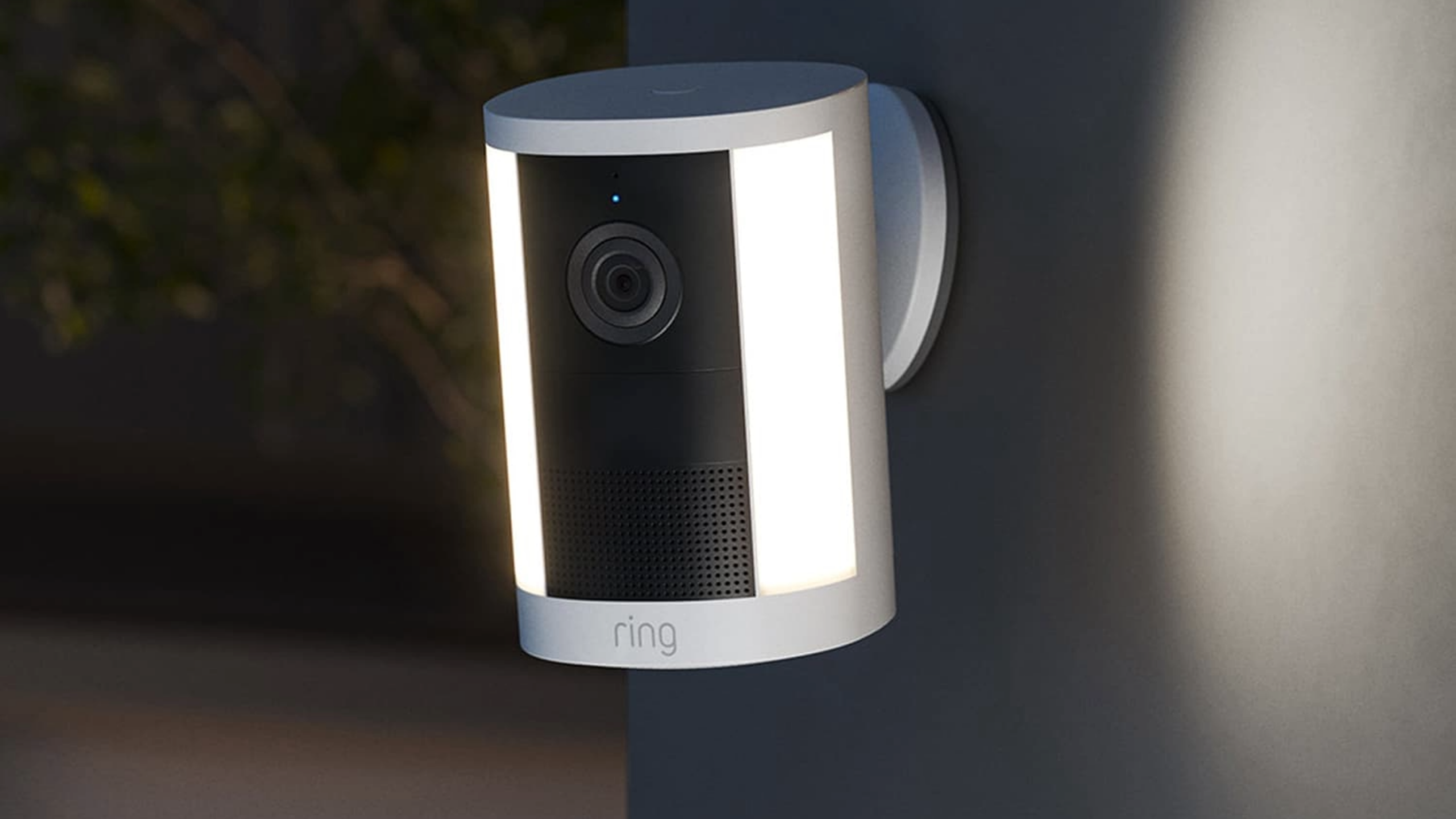 Ring outdoor spotlight camera in white mounted on a wall corner with its light strip lit