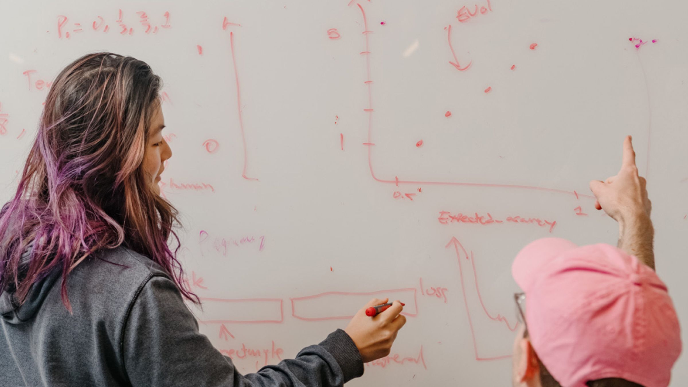 Two AI researchers working through equations and diagrams on a large office whiteboard