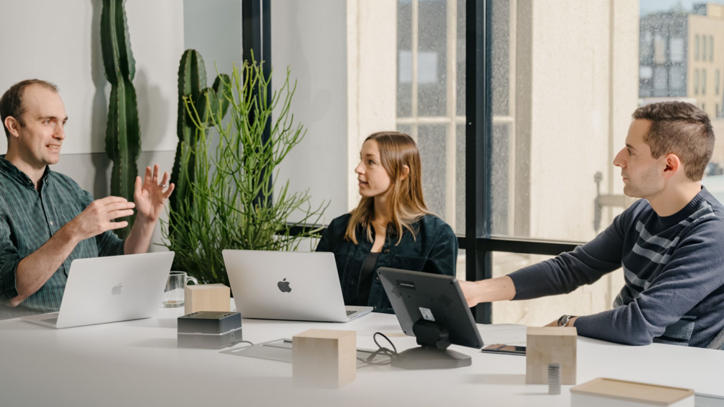 Three AI researchers in a bright meeting room comparing notes across open laptops