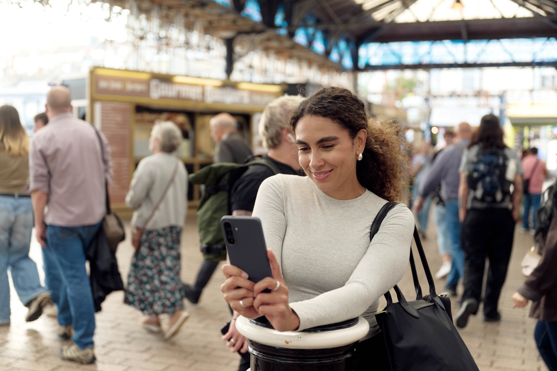 Woman smiling at her smartphone inside a busy covered Victorian market hall