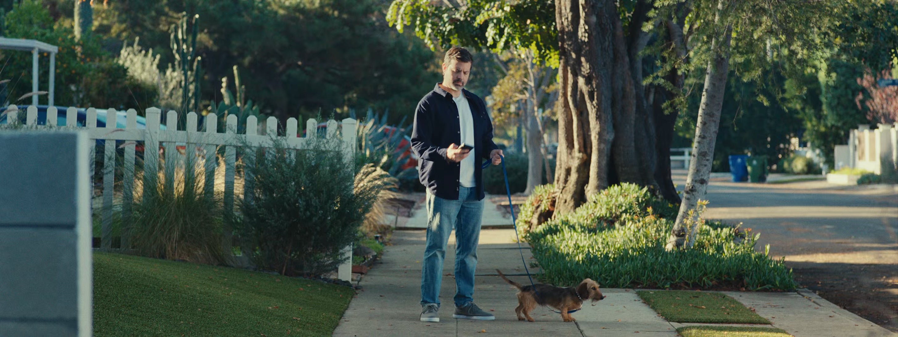 Man checking his phone on a suburban front path with a Ring doorbell installed at the door