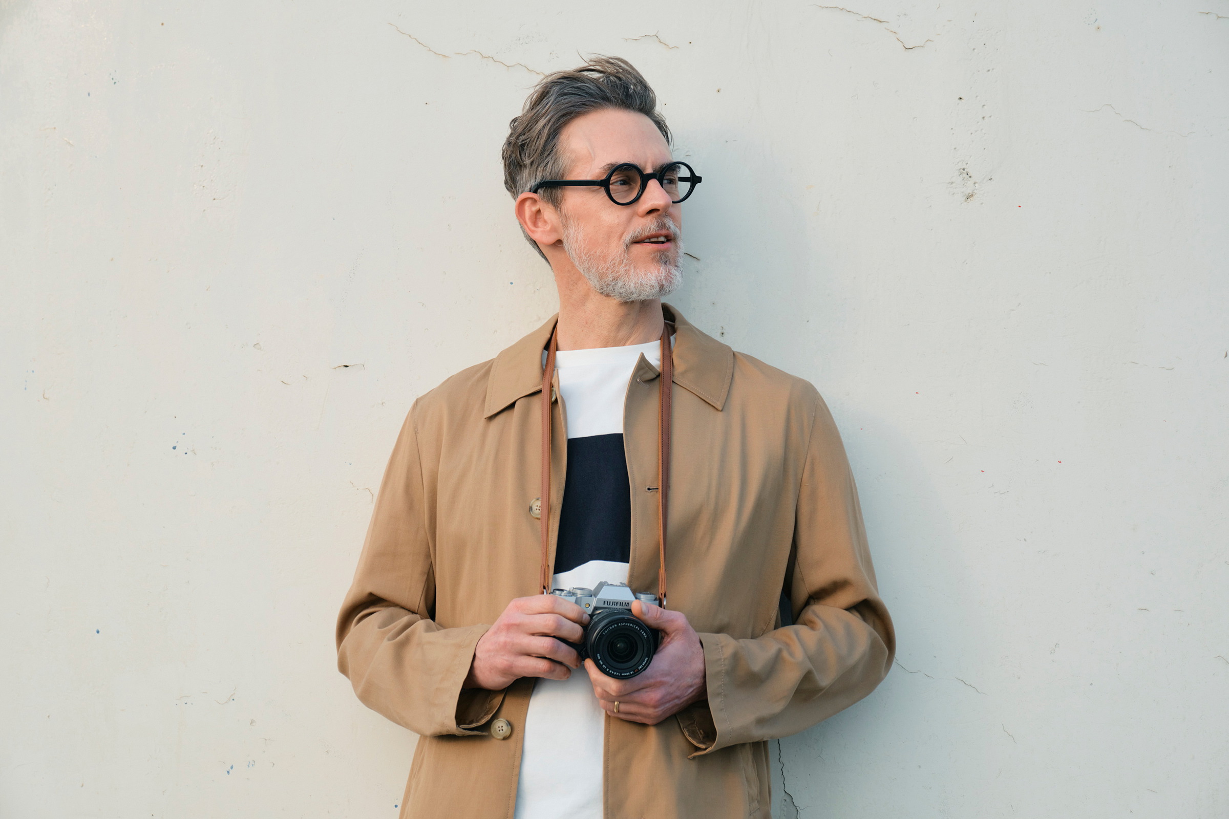 Photographer holding the silver Fujifilm X-T50 with XF16-50mm lens against a pale wall